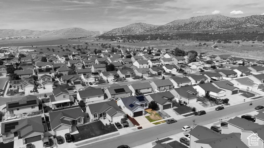 Aerial perspective featuring a single-family residence with roof-mounted solar panels, an attached two-car garage, and a concrete driveway, set against a mountainous landscape