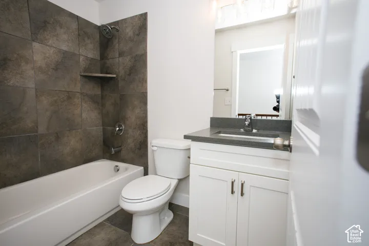 Bathroom featuring a white vanity cabinet with a dark solid-surface countertop, an integrated sink, large-format dark tile tub surround, and a chrome shower fixture