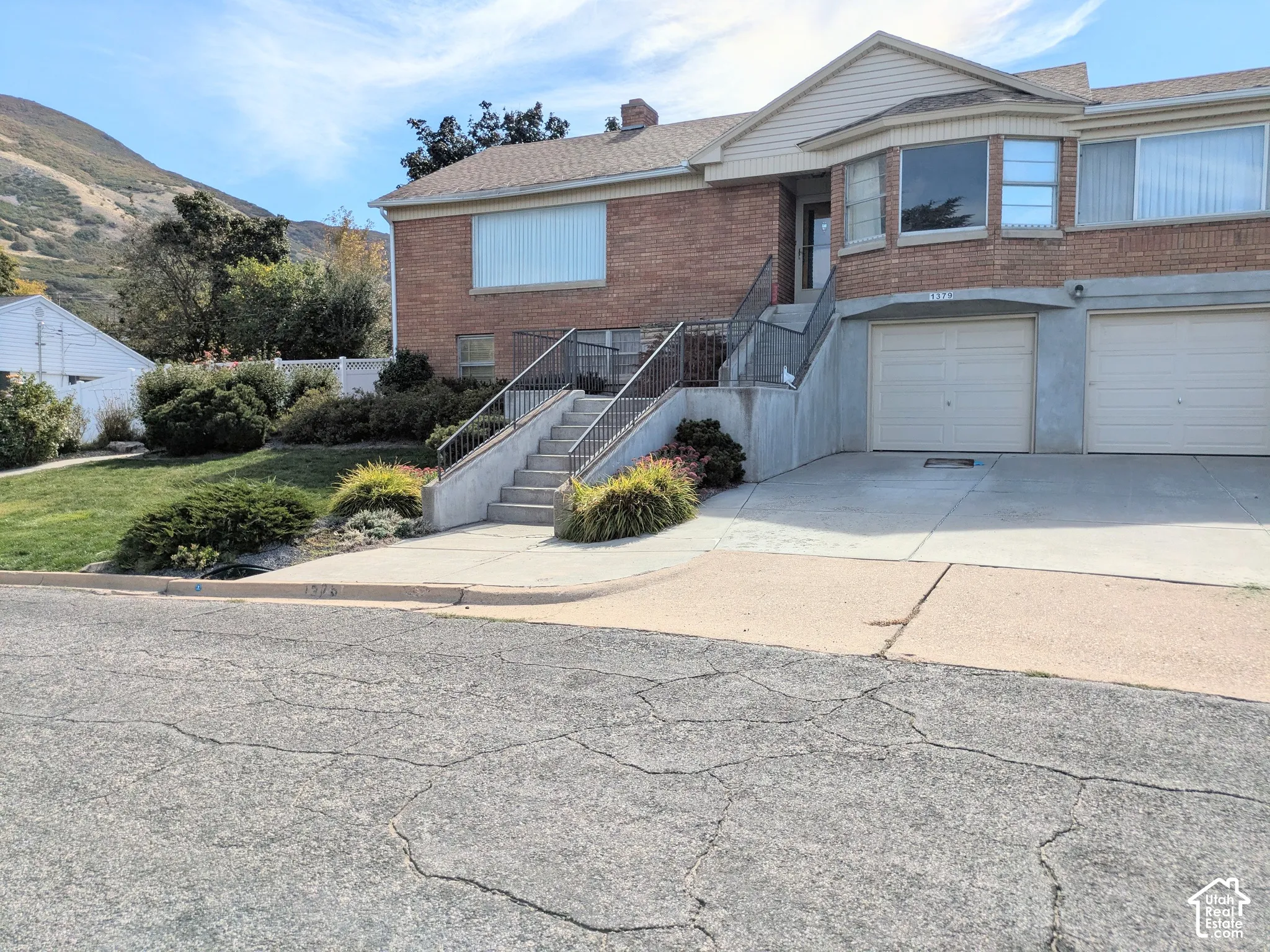 Brick and siding exterior featuring a multi-level concrete staircase with metal railings, dual garage doors, and mountain backdrop