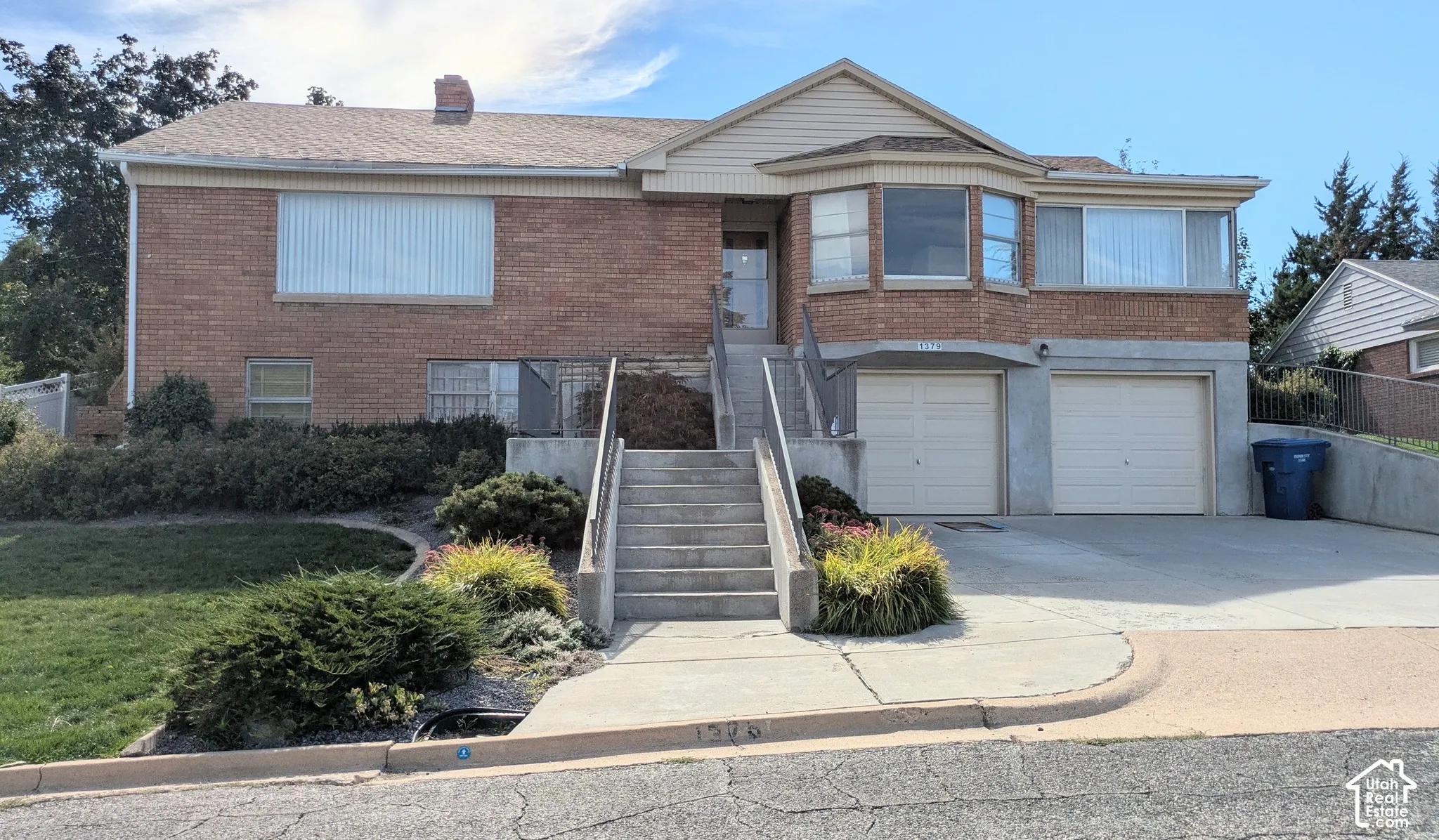 Brick exterior featuring a multi-level facade, bay window, two-car garage, concrete stairs with metal railings, and landscaped front yard