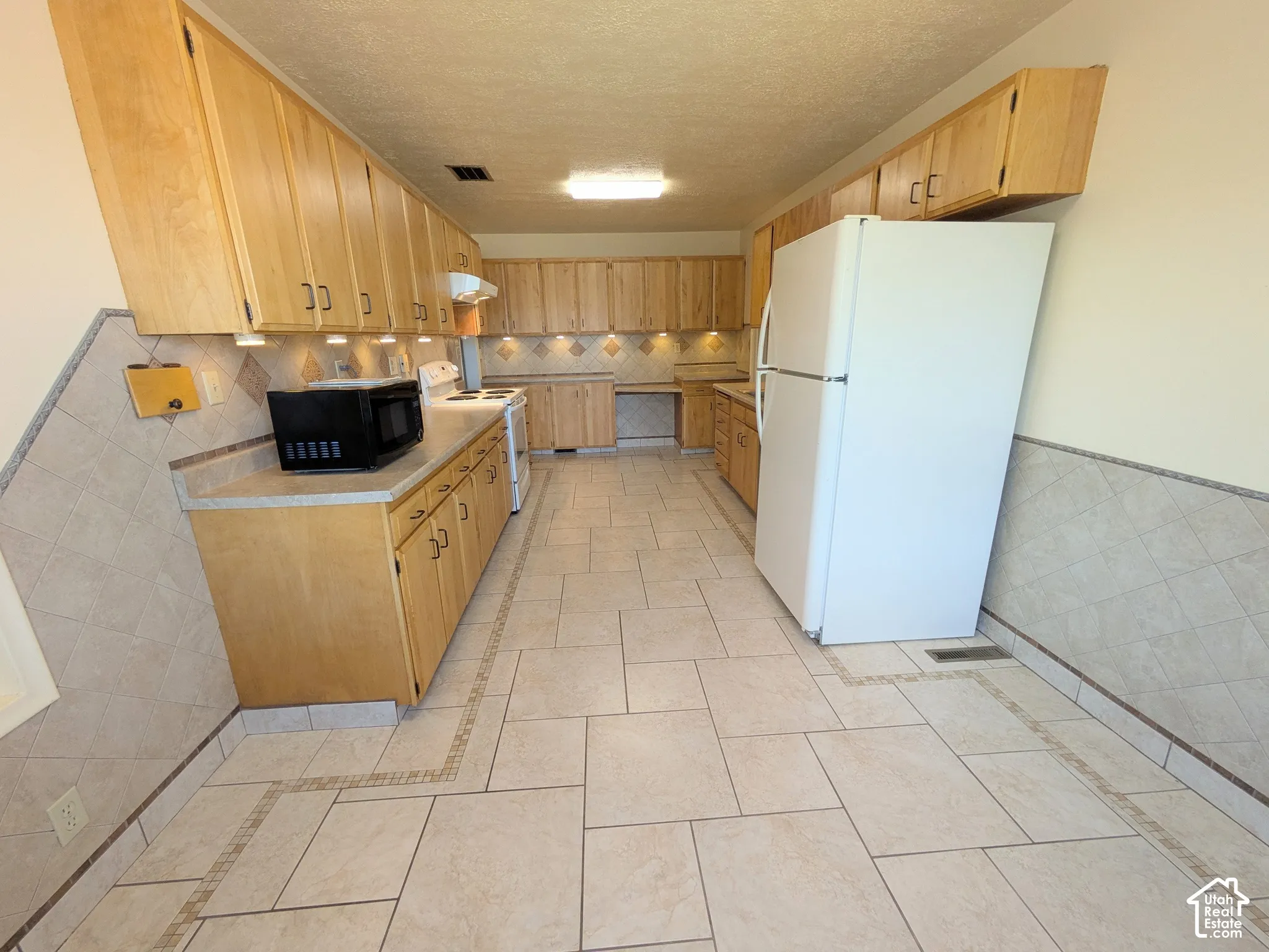 Kitchen featuring extensive light-wood cabinetry, neutral tile flooring, coordinated tile backsplash, and built-in task lighting