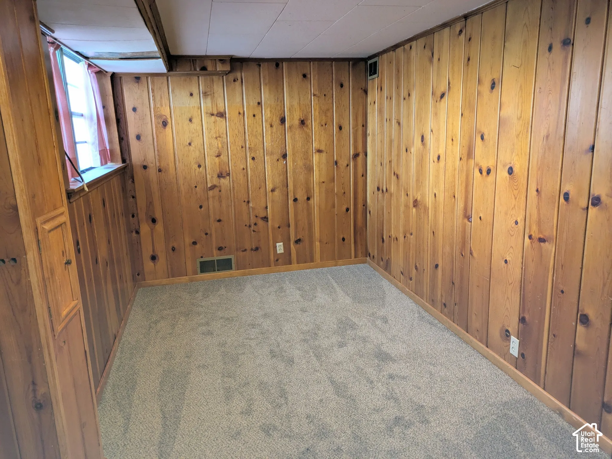 Knotty pine wood wall paneling, neutral carpeting, and a multi-pane window