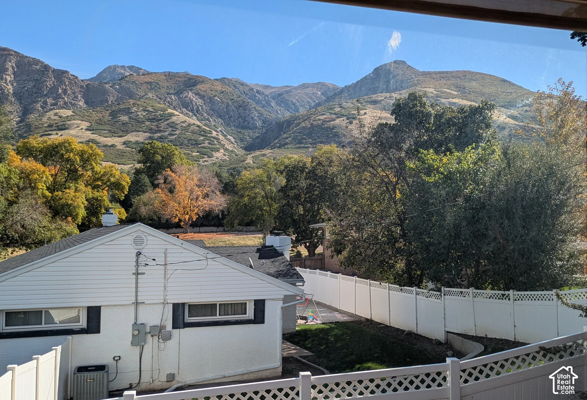 Mountainous backdrop featuring white vinyl fencing, mature deciduous trees, and a low-maintenance lawn