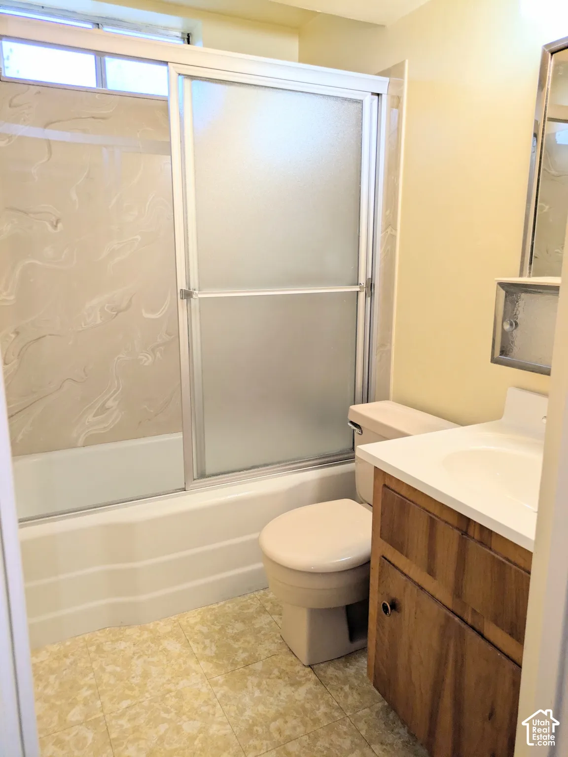 Bathroom featuring a tub-shower combination with frosted sliding doors and swirl-patterned wall surround, wood-finish vanity cabinet, solid-surface countertop with integrated sink, and wall-mounted medicine cabinet