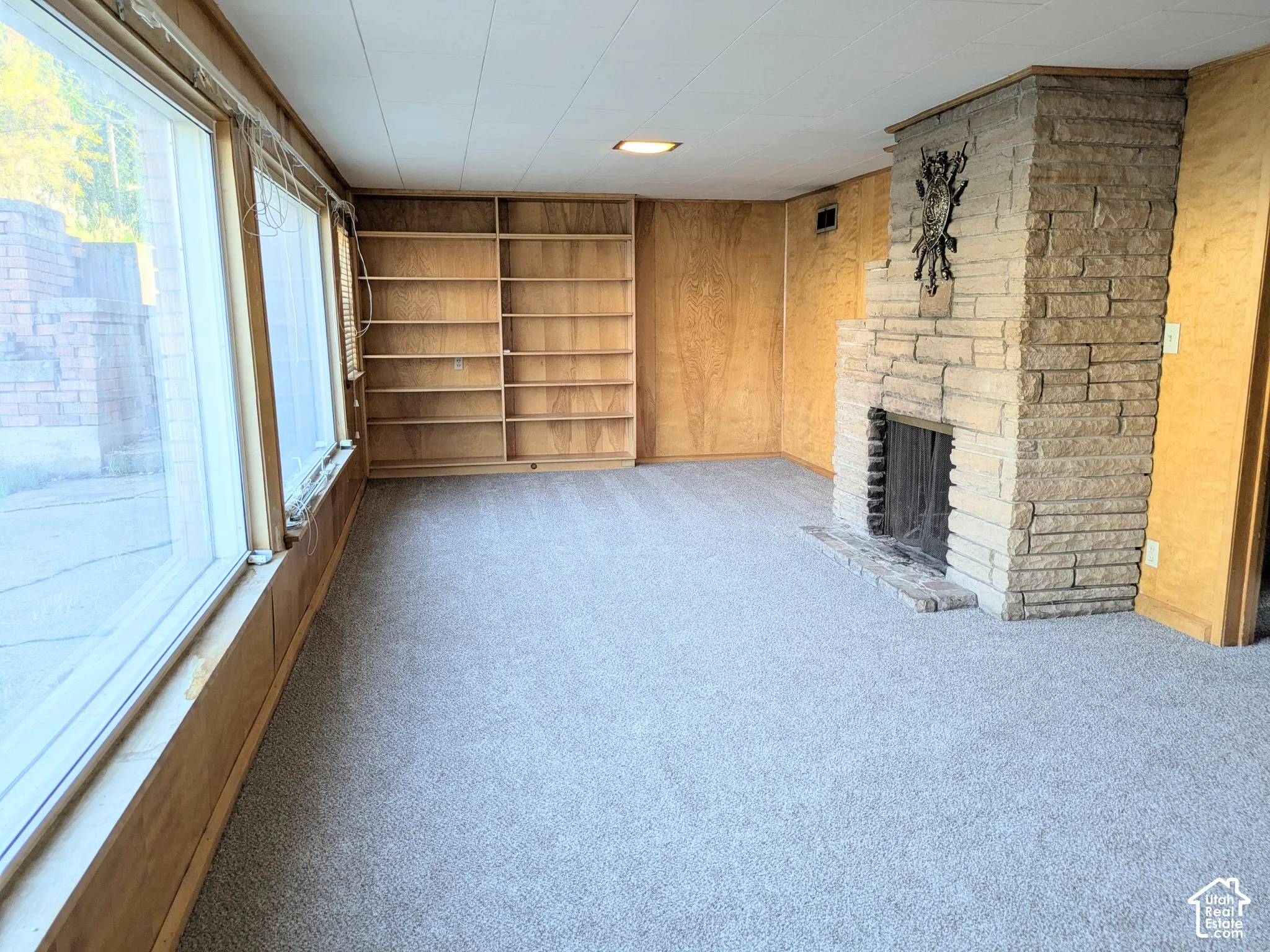 Floor-to-ceiling windows, built-in wooden shelving, and a floor-to-ceiling stone masonry fireplace with a metal screen