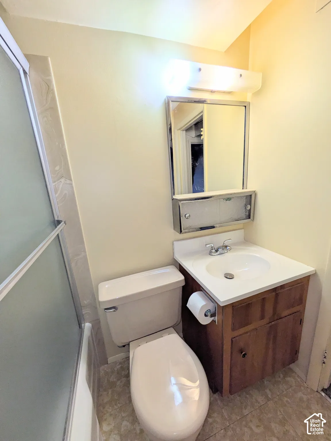 Full bathroom featuring a shower stall with frosted glass doors, wooden vanity cabinet, integrated sink with chrome faucet, and a wall-mounted medicine cabinet with mirror