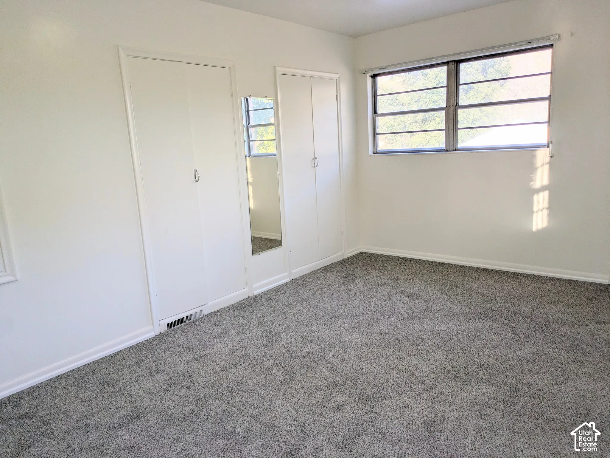 Interior space featuring neutral-toned carpeting, two sets of white double-door closets, a built-in wall mirror, and large windows