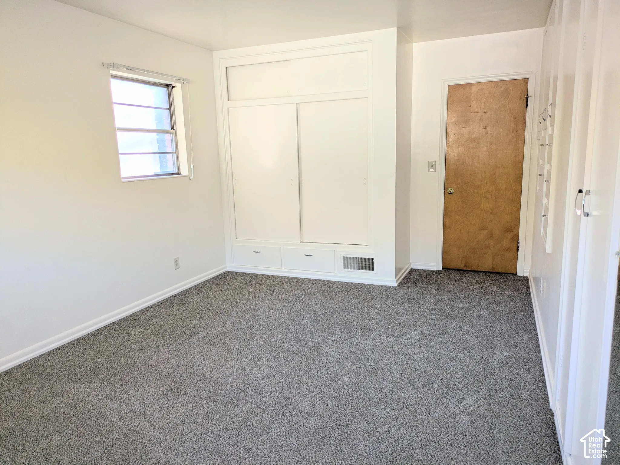 Neutral-toned carpet, built-in storage cabinetry with sliding doors and integrated drawers, and a single-pane window with grid inserts
