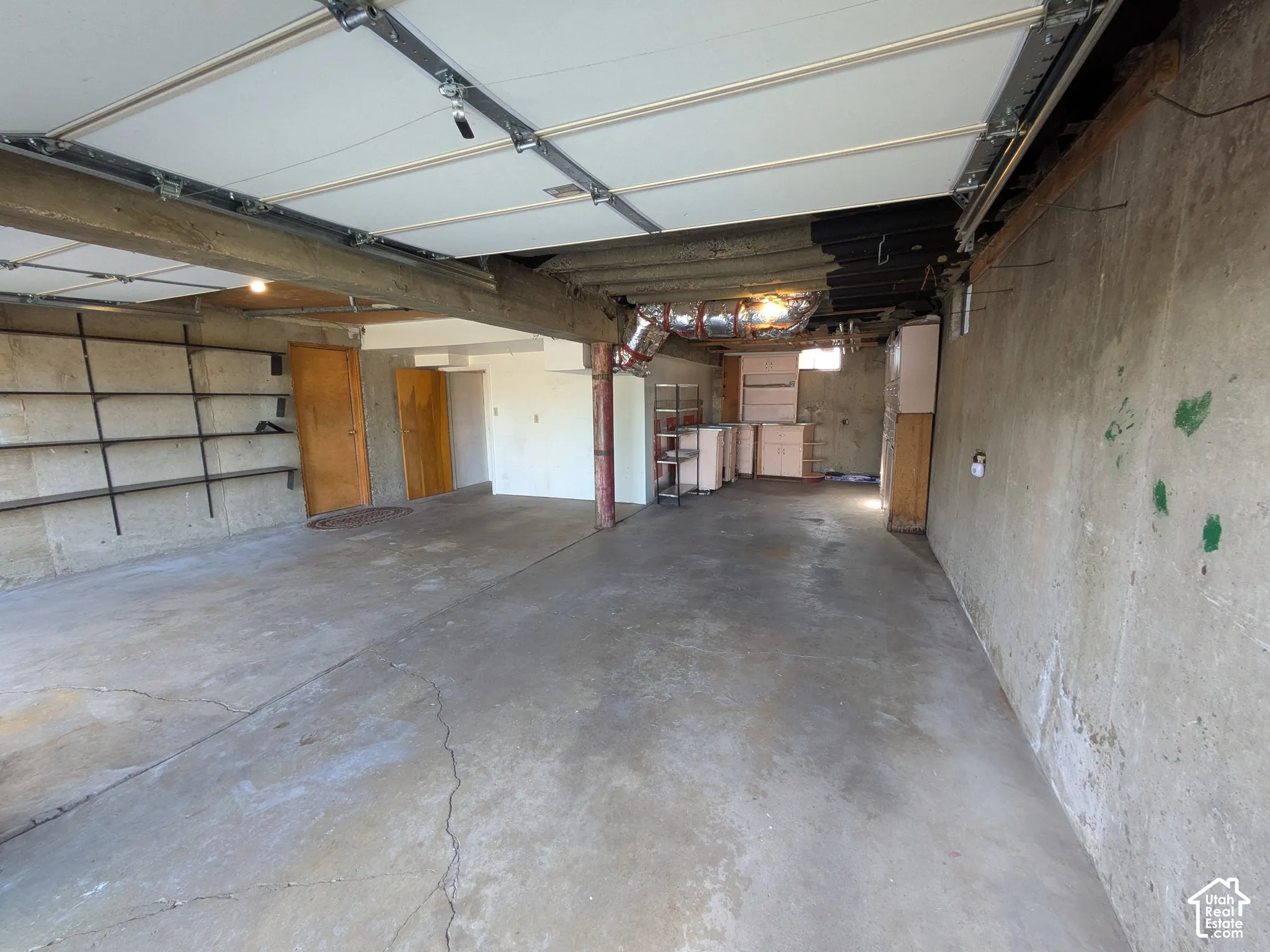 Garage interior featuring a concrete floor, structural wood-beam ceiling, attached wall-mounted metal shelving, and solid wood doors