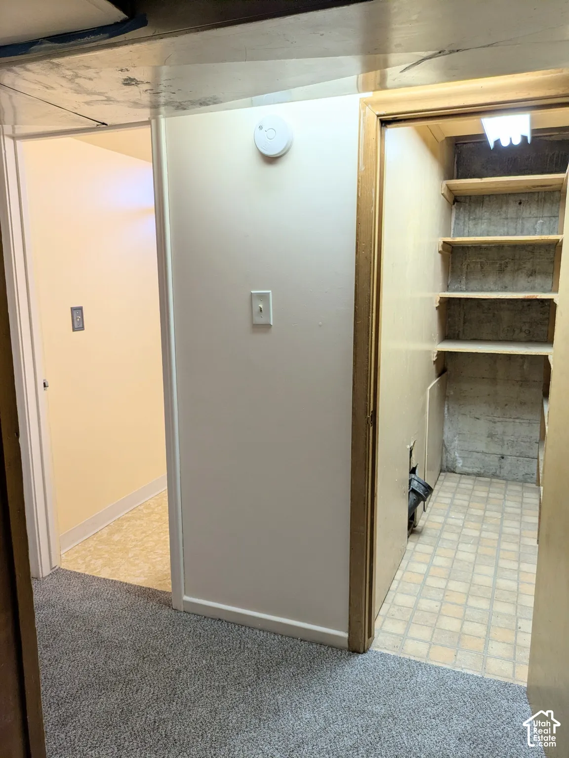 Storage space featuring built-in wooden shelving, concrete walls, and tiled flooring