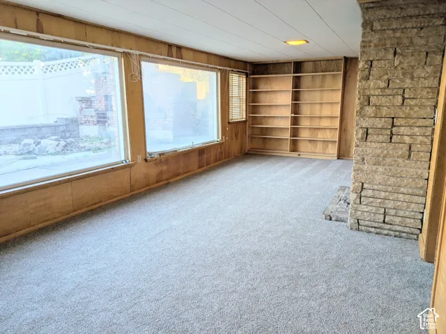 Expansive interior space featuring natural wood wall paneling, floor-to-ceiling built-in wooden shelving, a floor-to-ceiling textured stone fireplace, and large windows