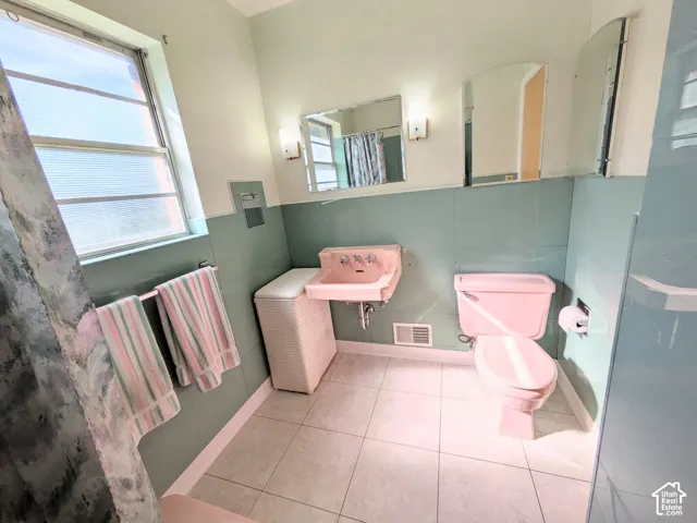 Wall-mounted sink, dual wall-mounted vanity mirrors, square floor tile, and pastel-toned tile wainscoting