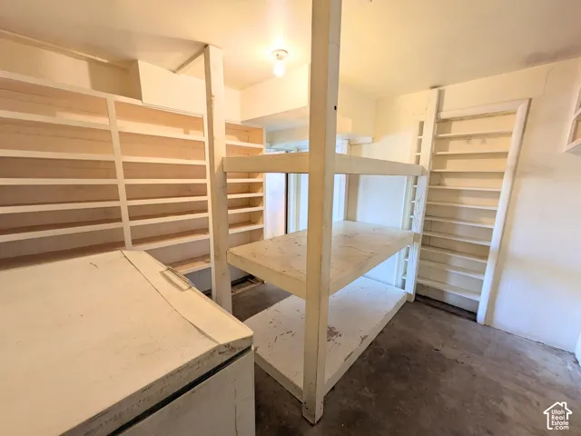 Storage room featuring multi-level built-in wooden shelving units, wall-mounted floor-to-ceiling shelving, and concrete flooring