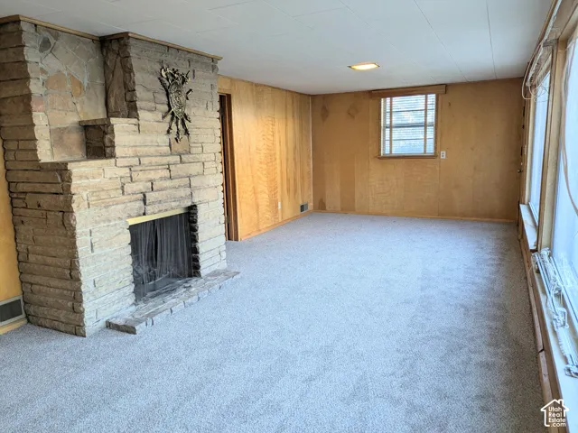 Floor-to-ceiling stone fireplace, wood-paneled walls, neutral carpeting, and large windows