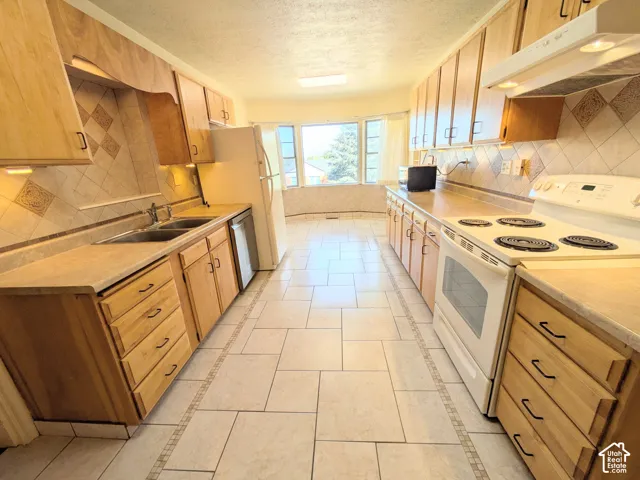 Kitchen featuring light-finish wood cabinetry, ceramic tile flooring with decorative inlay, diamond-patterned tile backsplash, and a multi-pane bay window