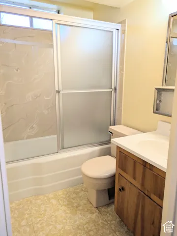 Bathroom featuring a tub-shower combination with frosted sliding doors and swirl-patterned wall surround, wood-finish vanity cabinet, solid-surface countertop with integrated sink, and wall-mounted medicine cabinet