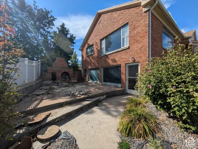 Red brick exterior, multi-level concrete patio, built-in brick fireplace, and white vinyl privacy fencing