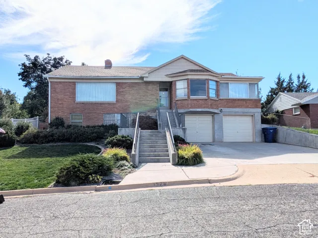 Brick exterior residence featuring a front-facing attached two-car garage, concrete driveway, bay window, and central staircase with concrete railings