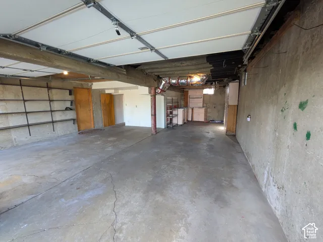 Garage interior featuring a concrete floor, structural wood-beam ceiling, attached wall-mounted metal shelving, and solid wood doors