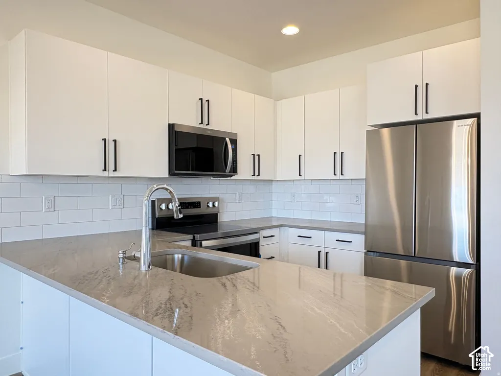 Kitchen featuring white shaker-style cabinetry, matte black hardware, quartz countertops, stainless steel appliances, and a subway tile backsplash
