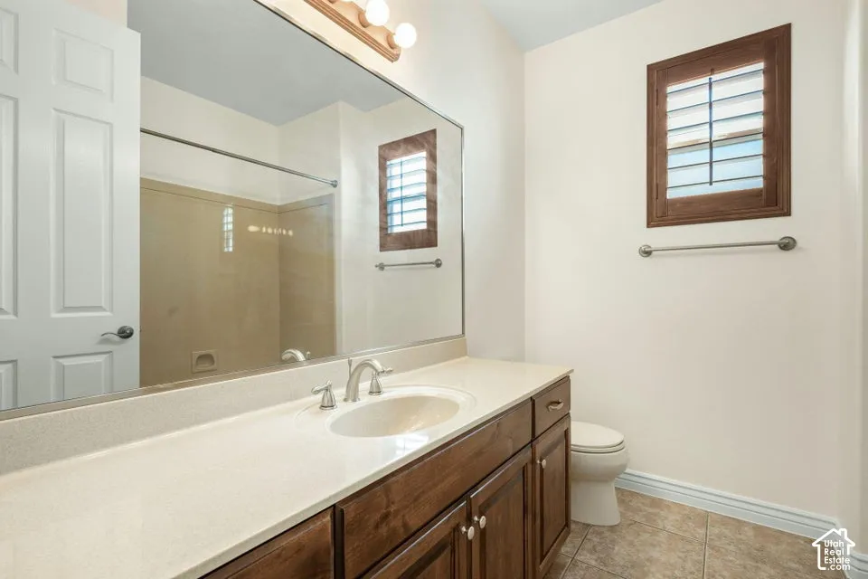 Bathroom featuring a stained wood vanity with a solid-surface countertop, an integrated sink, a full-width mirror, and a window with custom wood shutters