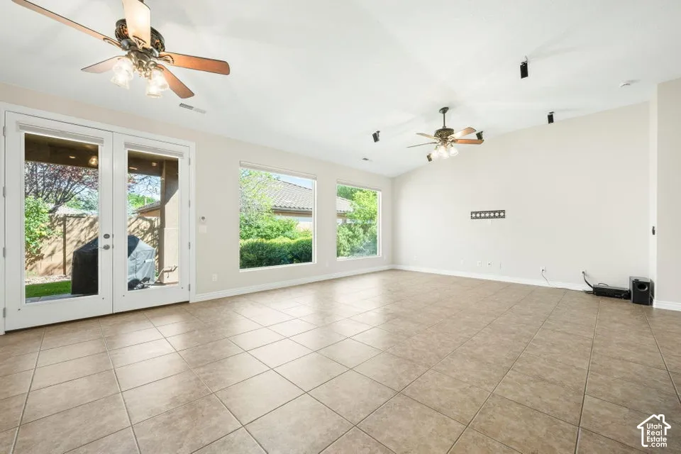 Neutral-toned interior space featuring vaulted ceilings, large picture windows, tile flooring, dual ceiling fans with integrated lighting, and glass-paned double doors