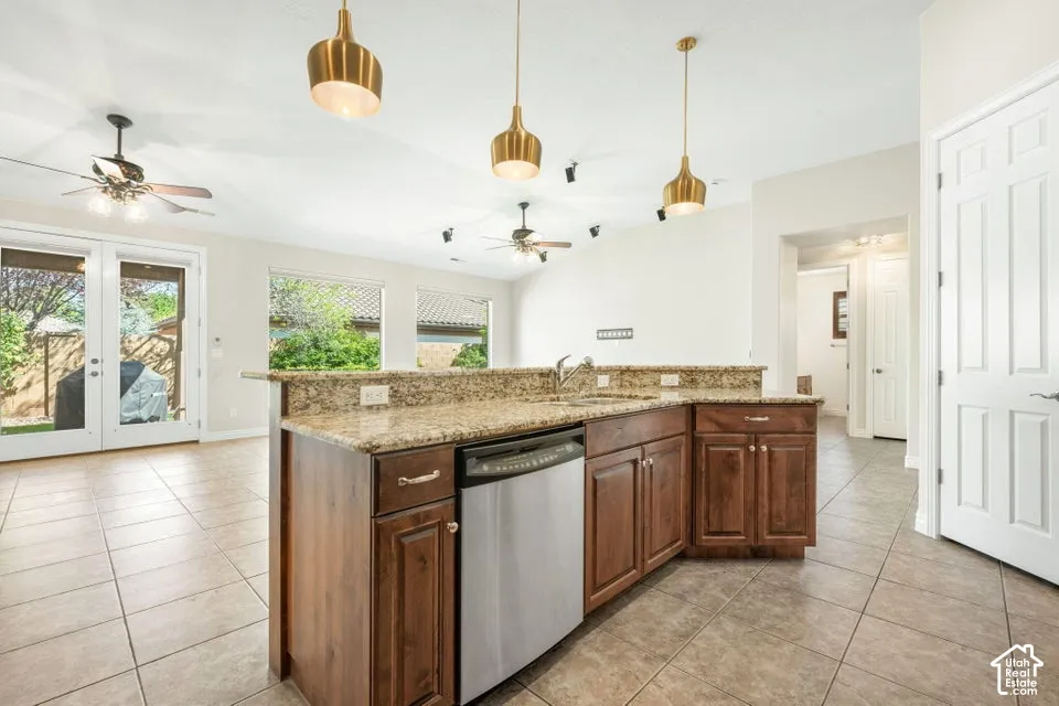 Kitchen featuring a tiered stone-surface island, wood-finish cabinetry, stainless steel dishwasher, tile flooring, and metallic pendant lighting