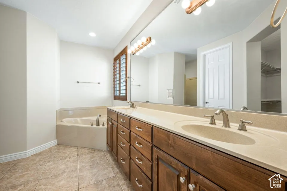 Dual-sink vanity with wood-finish cabinetry, solid-surface countertop, full-width mirror, soaking tub, and tile flooring