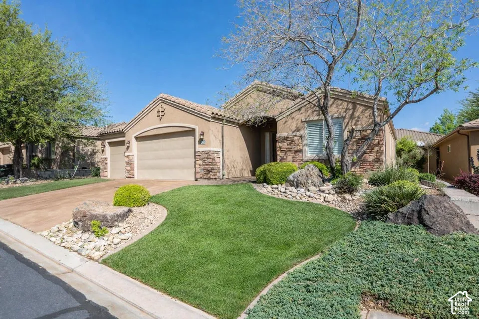 Stucco and stone veneer exterior featuring an attached three-car garage, concrete driveway, and xeriscaped front yard with curated landscape rock and mature shrubbery