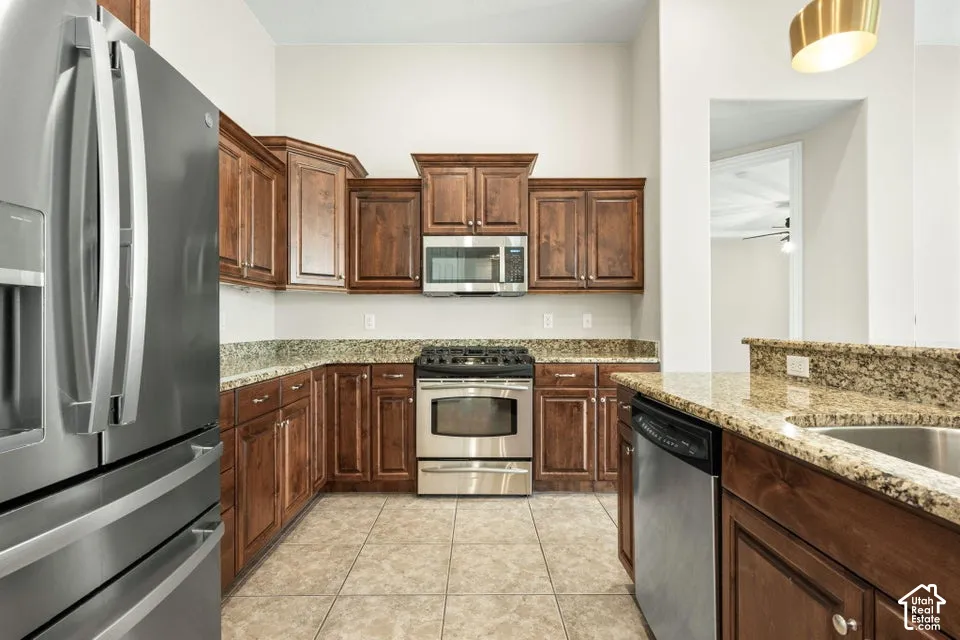 Kitchen featuring stained wood cabinetry, stone-finish countertops, stainless steel appliances, tile flooring, and a pendant light fixture