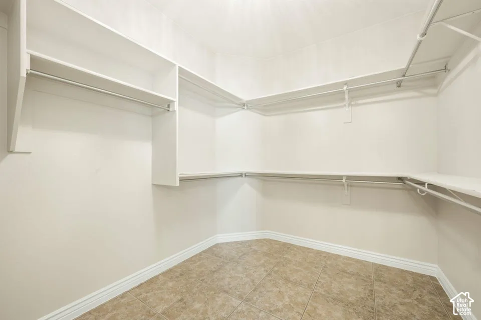 Walk-in closet featuring tiered white built-in shelving, metal garment rods, and neutral-toned tile flooring