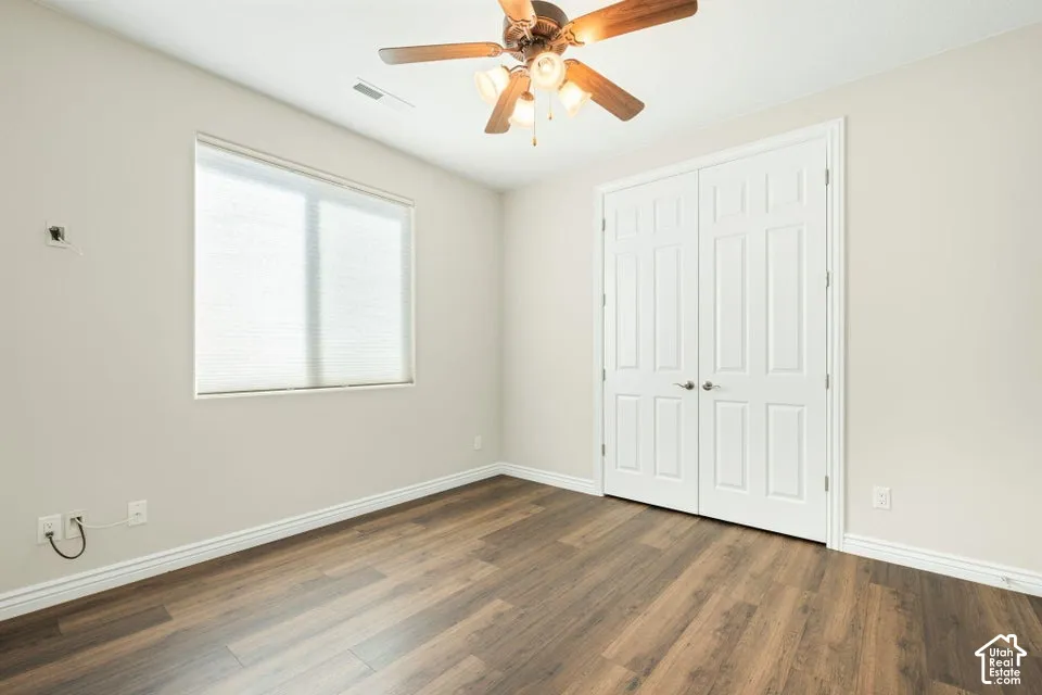 Room featuring wood-finish flooring, a neutral color palette, double-door closet, multi-light ceiling fan, and window with built-in blinds