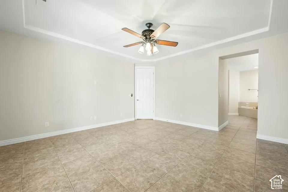 Room featuring a tray ceiling, ceiling fan with integrated lighting, neutral wall paint, and ceramic tile flooring