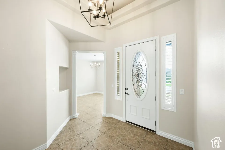 Entry featuring tile flooring, a geometric cage chandelier, a tray ceiling, an oval leaded glass front door with sidelights, and a recessed wall niche with a decorative column