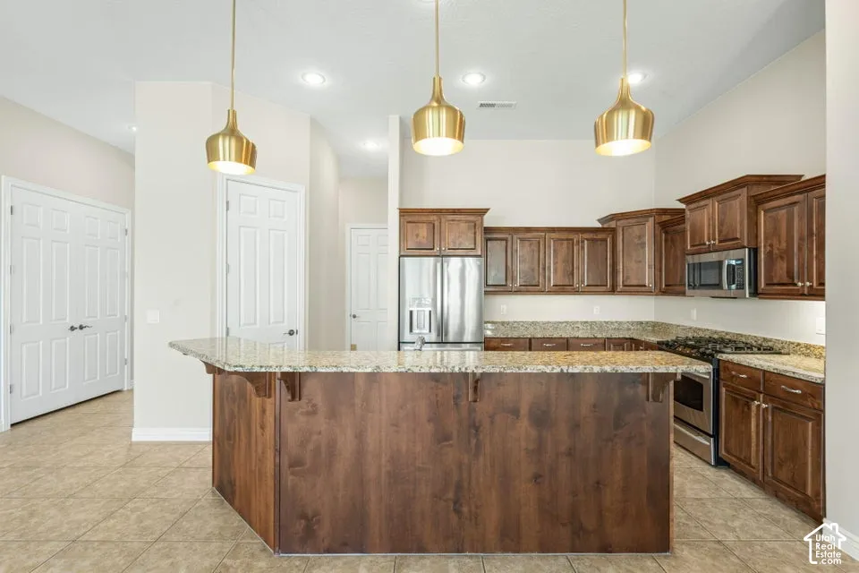 Kitchen featuring a wraparound stone countertop breakfast bar, stained wood cabinetry, stainless steel appliances, and three metallic pendant light fixtures
