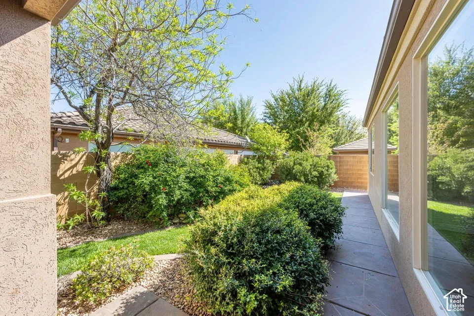 Landscaped side yard featuring a concrete paver walkway, mature shrubs, trees, and a masonry perimeter wall