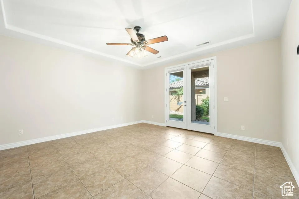 Tray ceiling with inset lighting, neutral-toned tile flooring, and glass-paneled double doors featuring external access