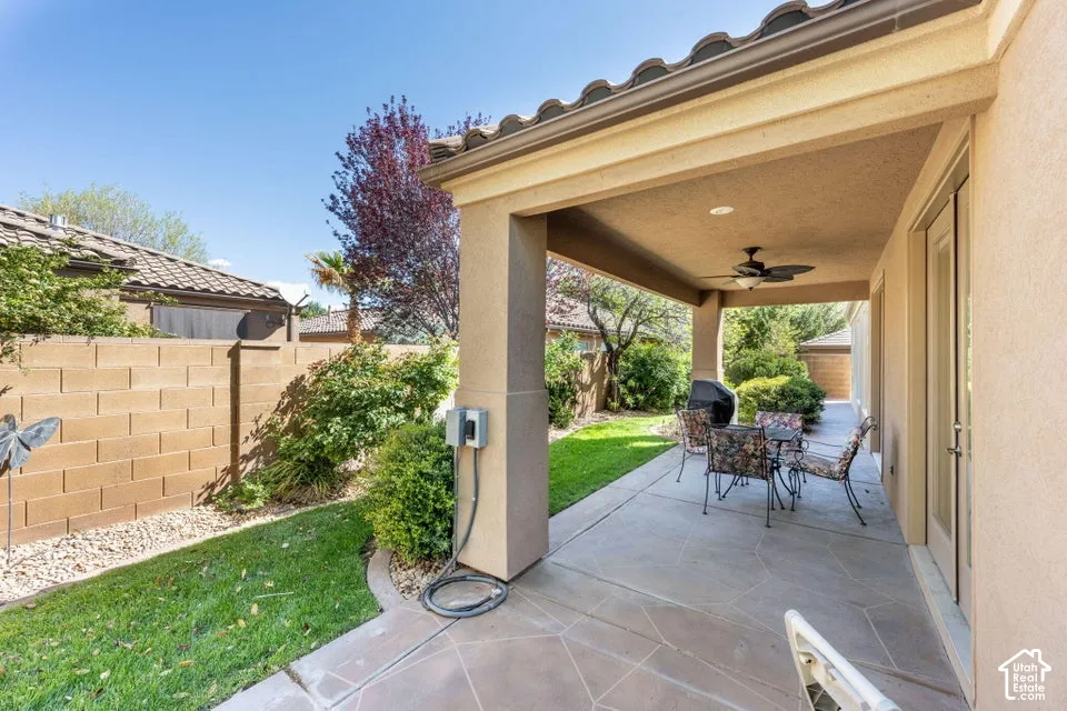 Covered patio featuring concrete paving, stucco columns, integrated ceiling lighting, a built-in ceiling fan, and surrounding masonry wall fencing