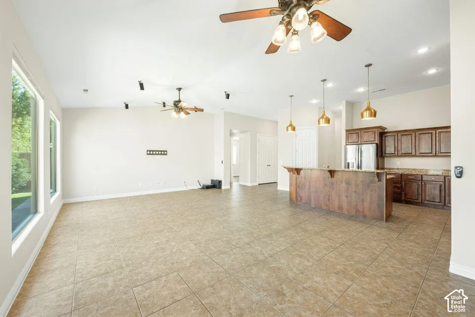 Open-concept area featuring tile flooring, ceiling fans, recessed lighting, and kitchen cabinetry with a breakfast bar