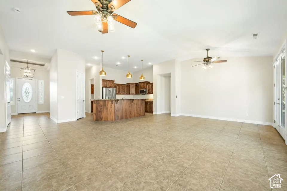 Open-concept interior featuring large-format tile flooring, vaulted ceilings, wooden cabinetry with stone-topped kitchen island, recessed lighting, and multiple ceiling fans