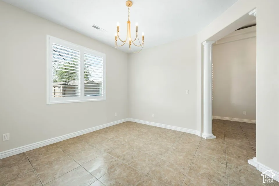 Room featuring neutral-toned tile flooring, white plantation shutters, an arched opening accented with a decorative column, and a multi-arm chandelier
