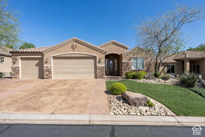 Stucco exterior featuring stacked stone accents, concrete tile roof, attached three-car garage, and manicured landscaping with rock hardscaping
