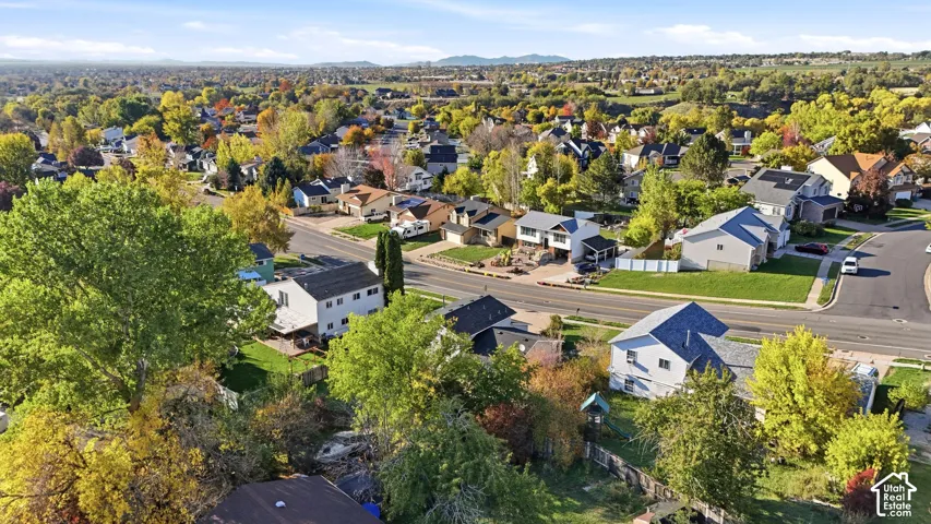 Aerial perspective of the residential area featuring mature trees, paved streets, manicured lawns, and distant mountain topography