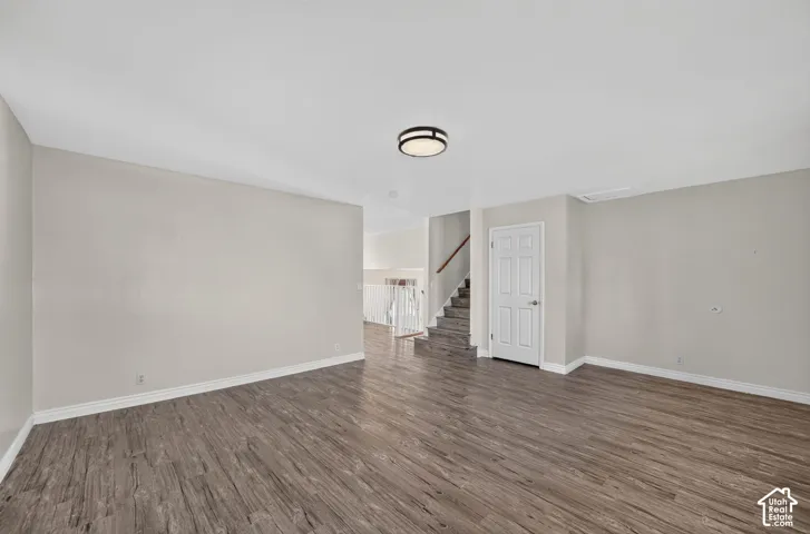 Neutral-toned interior space featuring wood-finish flooring, a flush-mount ceiling light, and a staircase with a wooden handrail and white balusters