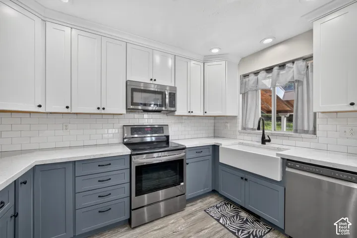 Kitchen featuring two-tone shaker-style cabinetry, quartz countertops, white subway tile backsplash, stainless steel appliances, and a farmhouse-style apron sink with a matte black faucet