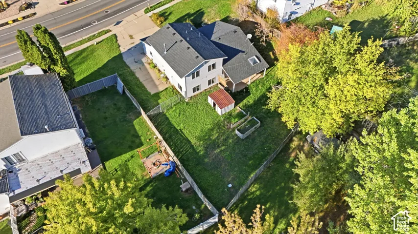 Aerial perspective of a multi-level residence featuring a fenced backyard, detached storage shed, asphalt shingle roofing, and established trees