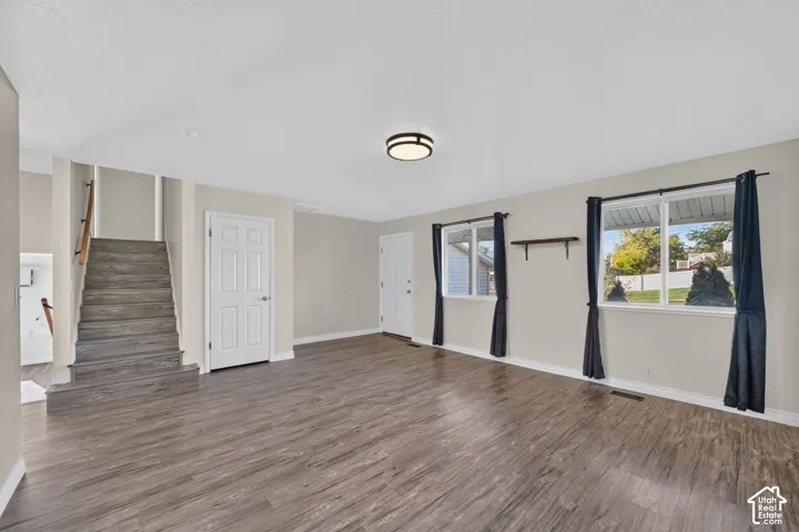 Open-concept interior space featuring wood-finish flooring, dual windows with natural light, staircase with wood-finish treads, and a flush-mount circular light fixture