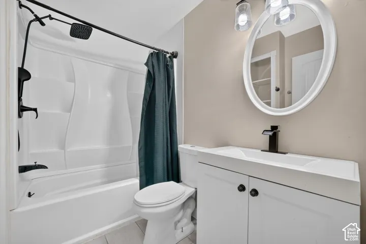 Bathroom featuring a white vanity cabinet with a rectangular basin, matte black waterfall faucet, oval wall-mounted mirror, and a tub-shower combination with a matte black rainfall showerhead