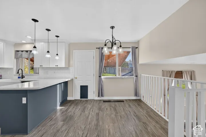 Kitchen featuring white upper cabinetry, a dual-tone blue lower island with stone-finish countertops, subway tile backsplash, three glass pendant lights, and wood-finish flooring
