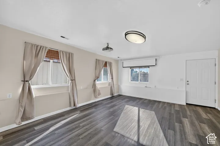 Interior room featuring wood-finish flooring, three windows with blinds, a ceiling-mounted projector, and a retractable projection screen